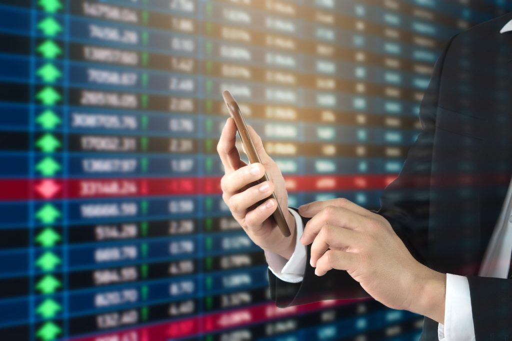 Dłoń z telefonem na tle tabeli notowań forex