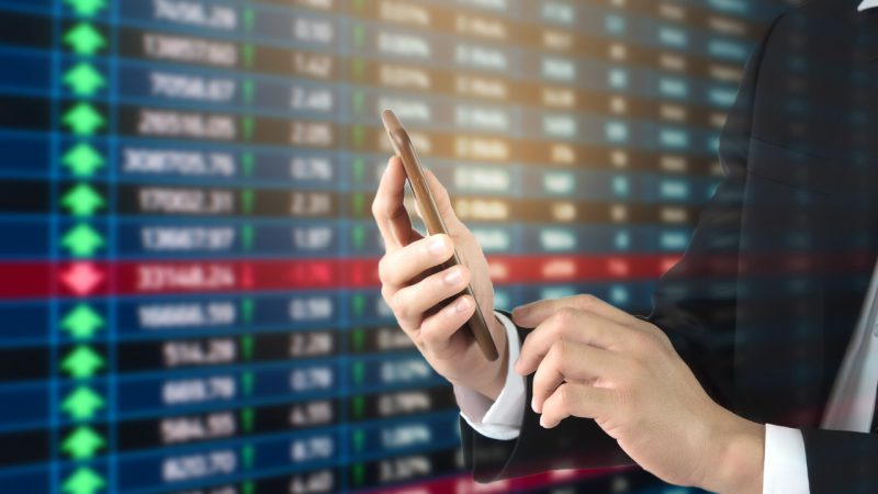 Dłoń z telefonem na tle tabeli notowań forex